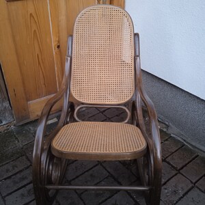 Peut inclure: Une chaise ber&ccedil;ante en bois brun avec un si&egrave;ge et un dossier en osier tress&eacute;. La chaise a un design incurv&eacute; et est faite de bois naturel.