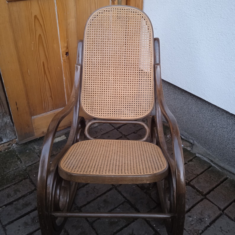 Peut inclure: Une chaise ber&ccedil;ante en bois brun avec un si&egrave;ge et un dossier en osier tress&eacute;. La chaise a un design incurv&eacute; et est faite de bois naturel.