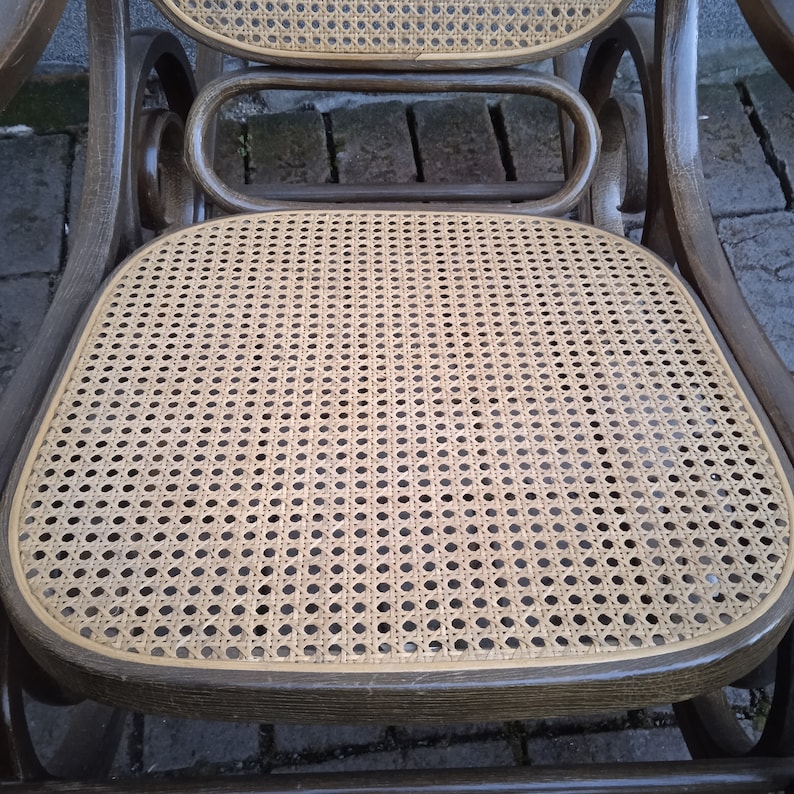 Peut inclure: Une chaise ber&ccedil;ante en bois brun avec un si&egrave;ge et un dossier en osier tress&eacute;. La chaise a un dossier et des accoudoirs incurv&eacute;s, et le si&egrave;ge est l&eacute;g&egrave;rement inclin&eacute;.
