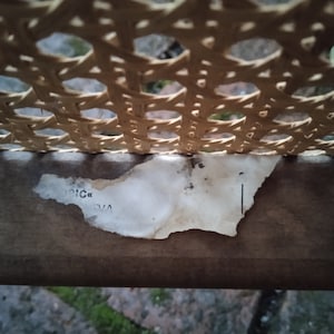 Peut inclure: Gros plan d'une chaise en rotin tress&eacute; avec une &eacute;tiquette en papier d&eacute;chir&eacute;e qui indique "V/A" et "RIC" sur le dessous de la chaise.