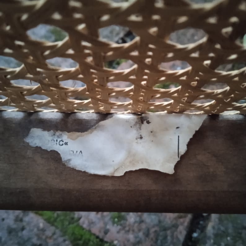 Peut inclure: Gros plan d'une chaise en rotin tress&eacute; avec une &eacute;tiquette en papier d&eacute;chir&eacute;e qui indique "V/A" et "RIC" sur le dessous de la chaise.