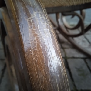 Peut inclure: Gros plan sur un bras de chaise ber&ccedil;ante en bois avec une finition craquel&eacute;e et patin&eacute;e. Le bois est brun fonc&eacute; et pr&eacute;sente un grain naturel. La finition montre des signes d'&acirc;ge et d'usure.