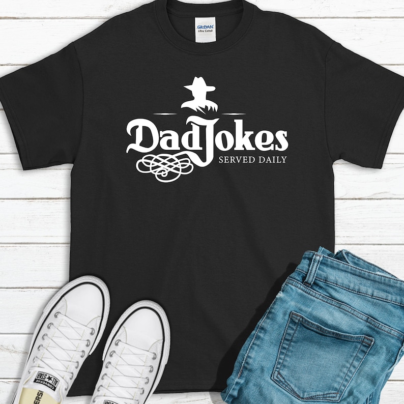 A fun design that says Dad Jokes all day that resembles a popular alcohol logo is shown on a black t-shirt in a white print. A great example of an end use for these designs.