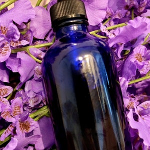 May include: A blue glass bottle with a dropper top, surrounded by purple flowers.