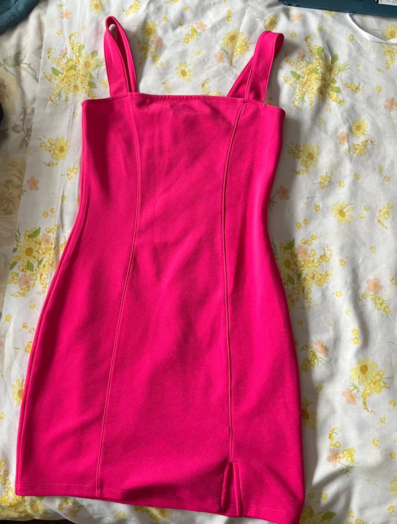 Puede incluir: Un vestido mini de color rosa fucsia sin mangas, con escote cuadrado y una peque&ntilde;a abertura en el dobladillo.