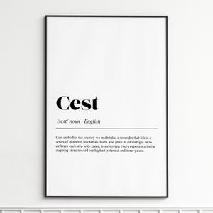 May include: A framed print with the word "Cest" in a bold, black serif font. Below, the definition reads "/sest/ noun English." The print includes a paragraph about cherishing moments and inner peace. The frame is black.
