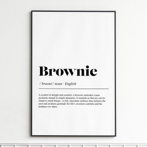 May include: A framed print with the word "Brownie" in bold black letters. Below, the phonetic pronunciation and the word "noun" are displayed. The text describes a brownie as a symbol of delight and comfort.