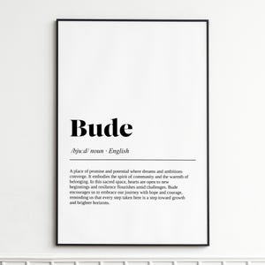 May include: A framed print featuring the word "Bude" in a bold, black font. The definition below describes a place of promise and potential. The print is set within a black frame, suitable for home decor.