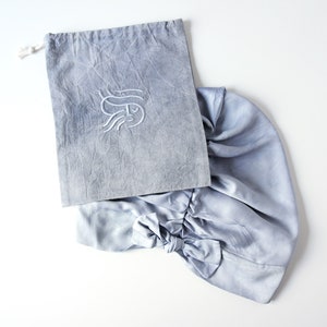 May include: A light blue fabric drawstring bag with a white embroidered design. The bag is made of a soft, textured material and has a gathered, ruffled appearance.