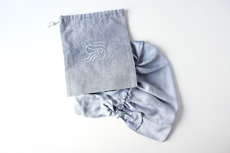 May include: A light blue fabric drawstring bag with a white embroidered design. The bag is made of a soft, textured material and has a gathered, ruffled appearance.