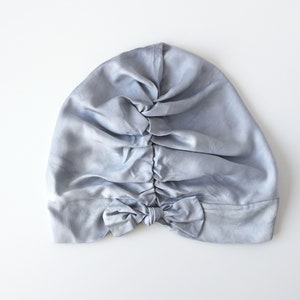 May include: A light blue satin sleep cap with a bow at the back.