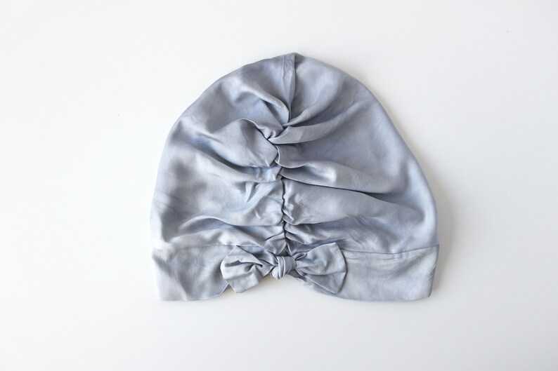 May include: A light blue satin sleep cap with a bow at the back.