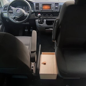 May include: The interior of a black van with two black seats and a wooden storage box between them. The driver's seat is turned towards the passenger seat.