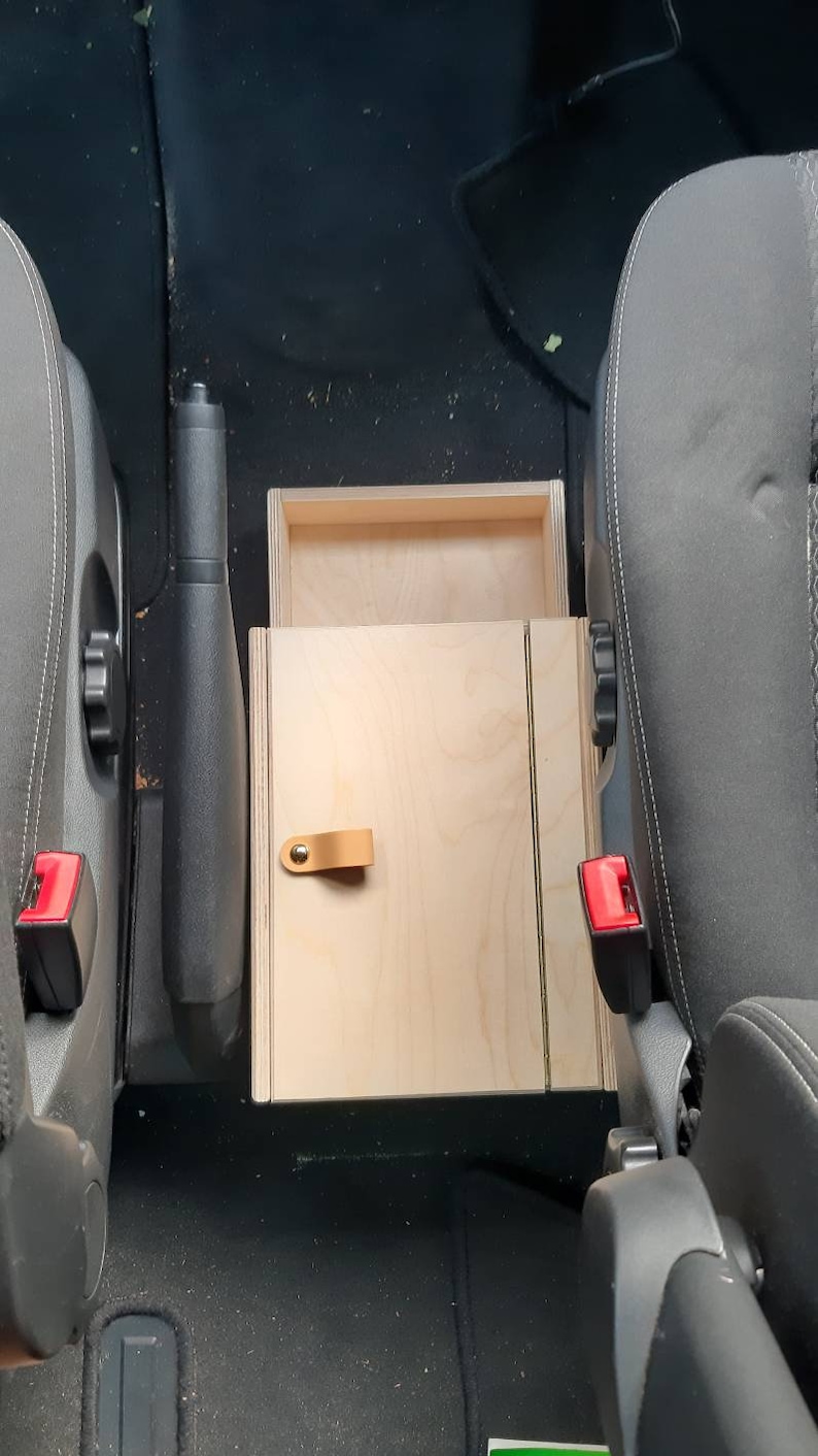 May include: A wooden storage box with a hinged lid and a leather handle. The box is installed in the center console of a car.