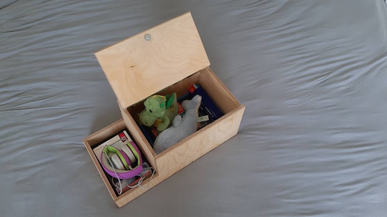 May include: A wooden box with a hinged lid, open to reveal a green and gray stuffed animal, a book, and a pair of purple headphones in a separate compartment.