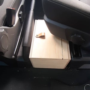 May include: A light wood storage box with a leather handle, installed between the front seats of a car.