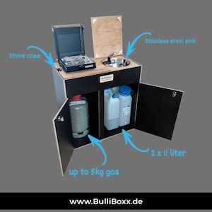 Op de afbeelding: Een zwart en houten kampeerkast met een roestvrijstalen spoelbak, kooktoestel en opslag voor gas en water. De unit bevat een Primus kooktoestel, twee 11-liter watercontainers en ruimte voor maximaal 5 kg gas.