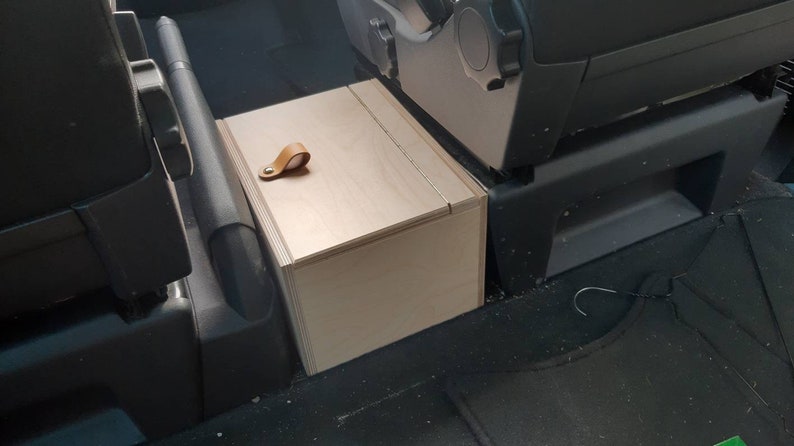 May include: A light wood storage box with a leather handle, installed in the back seat of a vehicle.