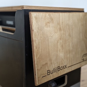 Op de afbeelding: Zwarte kast met een houten deur waarop de tekst "_Bulli|Boxx_" en een kleine illustratie van een bestelwagen staat.