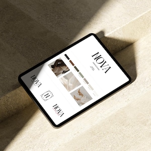 May include: A black tablet displaying the "NOVA Creative Studio" logo and design samples. The screen shows a logo, color palette, and images. The tablet is angled on a light-colored surface, with shadows.
