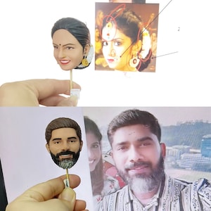 May include: Two custom-made cake toppers, one depicting a woman with dark hair and a red bindi, and the other depicting a man with a beard. Both toppers are holding a small stick.