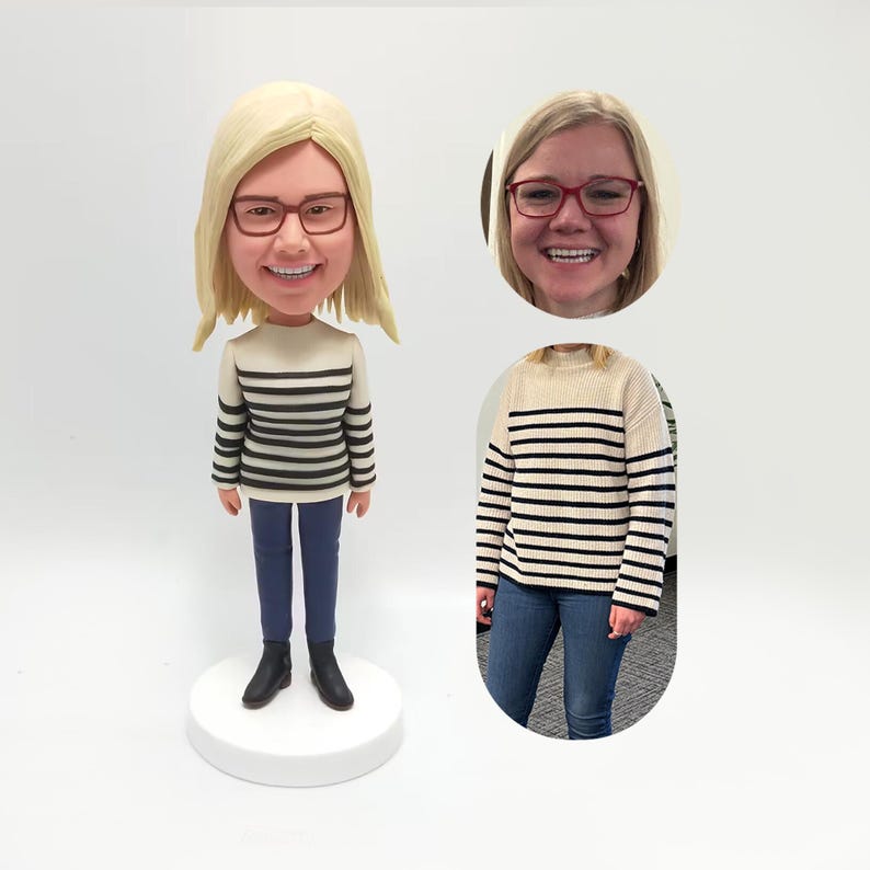 May include: A bobblehead doll of a person with blonde hair and glasses, wearing a cream-colored sweater with black horizontal stripes, blue jeans, and black boots. The doll is on a white base. An image of the person is in the background.