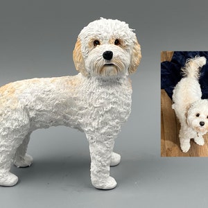 May include: A white and cream ceramic dog figurine. The figurine is standing on all four legs and has a fluffy, realistic texture. The dog has brown eyes and a black nose.