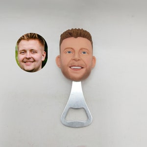 May include: A silver bottle opener with a 3D printed face of a person. The person has brown hair and is smiling.