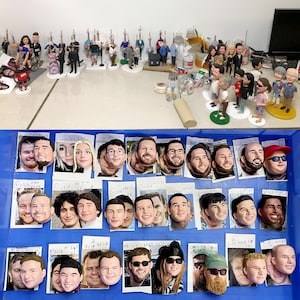 May include: A collection of miniature figurines of people, some wearing hats and glasses, arranged on a blue surface with white labels. The figurines are made of painted ceramic and are approximately 2 inches tall.