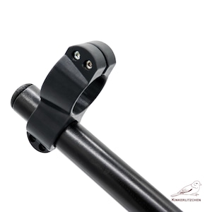 May include: A black motorcycle handlebar clamp with two silver screws. The clamp is attached to a black tube. The image is set against a white background. The logo "Kinkerlitzchen" is in the bottom right corner.