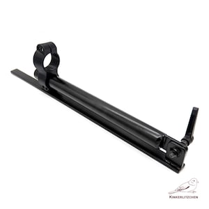 May include: A black metal rifle scope mount with a circular ring, a long cylindrical tube, and a rectangular base. The mount has a lever and a small screw. The image includes a logo of a bird and the text "KINKERLITZCHEN".