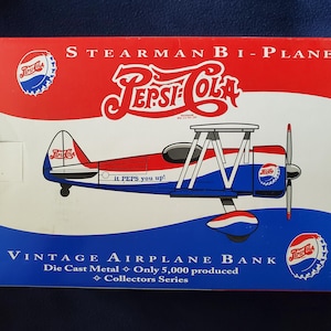 May include: A vintage red, white, and blue die-cast metal Stearman bi-plane airplane bank featuring the Pepsi-Cola logo. The bank has a red, white, and blue paint scheme and says "it PEPS you up!"  Vintage Airplane Bank, Die Cast Metal, Only 5,000 produced, Collectors Series.