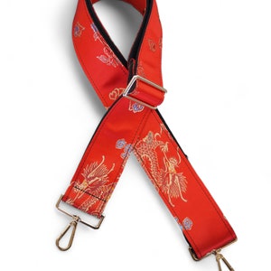 May include: Red guitar strap with a black backing and gold dragon pattern. The strap has two silver clasps.