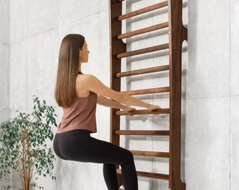 May include: A woman in a pink tank top and black leggings is using a wooden wall-mounted pull-up bar. The bar has 10 rungs and is made of dark wood.