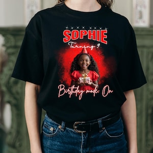 Może przedstawiać: Czarny t-shirt z czerwoną grafiką z napisem "Sophie Turning 9" i "Birthday mode: On". Grafika zawiera zdjęcie uśmiechniętej dziewczynki w czerwonej sukience trzymającej prezent, na urodziny.