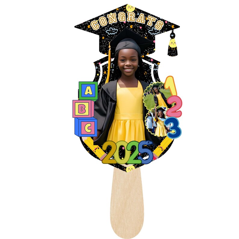 May include: Graduation photo prop featuring a young person in a yellow dress and graduation cap. The prop includes the word "CONGRATS", the year "2025", and colorful numbers and blocks. The prop is held by a wooden stick.