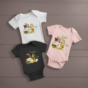 May include: Three white, pink and black baby onesies with a jungle animal theme. The onesies say "Wild One" with different titles above the text, including "Cousin", "Sister", and "Wild".