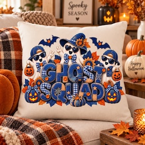 May include: A square throw pillow with a cream-colored background featuring a graphic of three ghosts wearing blue baseball caps and sunglasses. The text GHOST SQUAD is centered in blue, surrounded by orange pumpkins, autumn leaves, and bats.