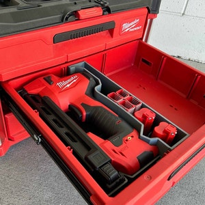 May include: A red Milwaukee Packout tool box with a drawer open, revealing a red and black Milwaukee cordless nail gun, two batteries, and a compartment for nails.