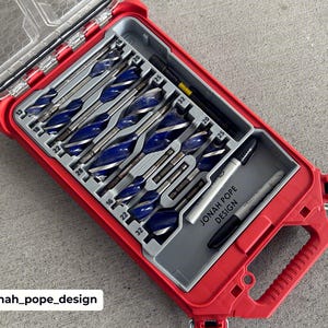 May include: A red toolbox with a clear lid, containing a set of blue and silver drill bits. The toolbox also holds a black marker and a silver pen. The text "JONAH POPE DESIGN" is printed on the gray interior.