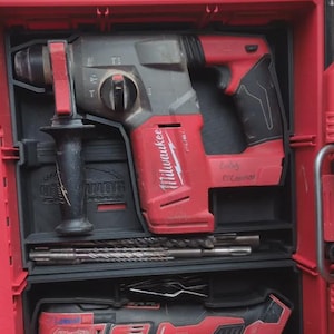 May include: A red and gray Milwaukee rotary hammer drill with a black handle and drill bits, stored in a red toolbox. The drill has the Milwaukee logo on the side.