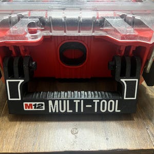 May include: A red and black tool case with a clear lid. The case has a black handle with the text "M12 MULTI-TOOL" printed on it.