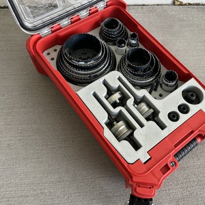 May include: A red plastic case with a clear lid, containing a variety of hole saw bits and other tools. The case is open and the tools are visible.