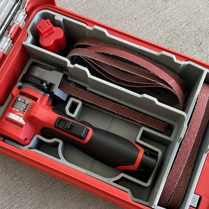 May include: A red and black power tool with a gray and red case. The tool is a belt sander and is surrounded by several brown sanding belts. The case has a clear lid.