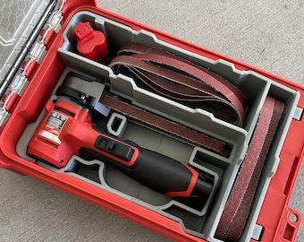 Puede incluir: Una herramienta eléctrica roja y negra con una caja gris y roja. La herramienta es una lijadora de banda y está rodeada de varias bandas de lijado marrones. La caja tiene una tapa transparente.