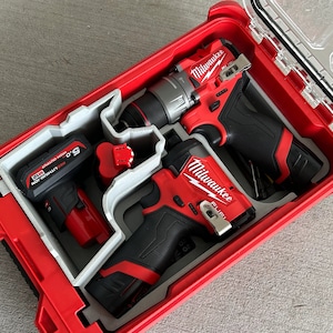 May include: Three Milwaukee power tools, a red and black drill, a red and black impact driver, and a red and black impact wrench, are stored in a red and gray hard plastic case with a clear lid.