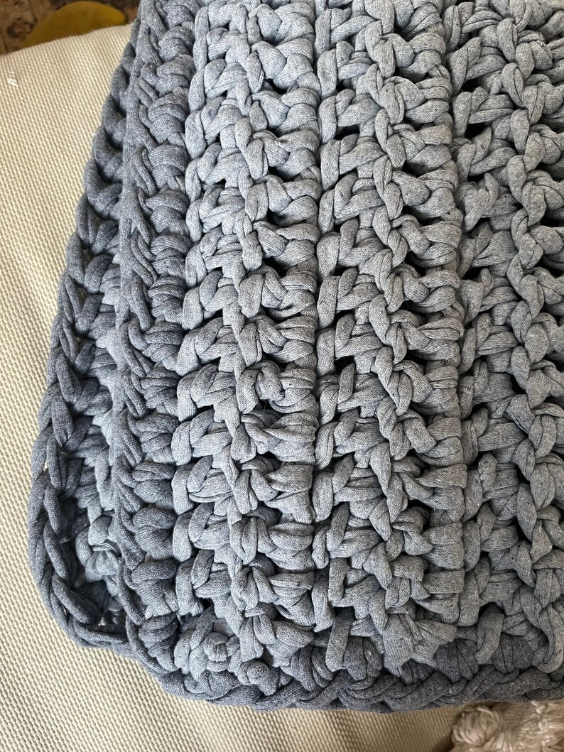 Puede incluir: Una manta de crochet gris con un patr&oacute;n texturizado. La manta est&aacute; hecha de hilo grueso y tiene una sensaci&oacute;n suave y acogedora.