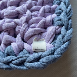 Puede incluir: Primer plano de un posavasos de crochet lavanda y azul con una etiqueta blanca que dice "ahava".