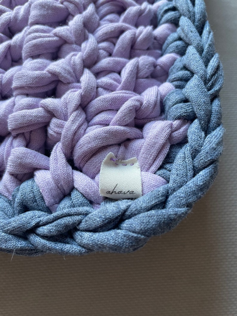 Puede incluir: Primer plano de un posavasos de crochet lavanda y azul con una etiqueta blanca que dice "ahava".