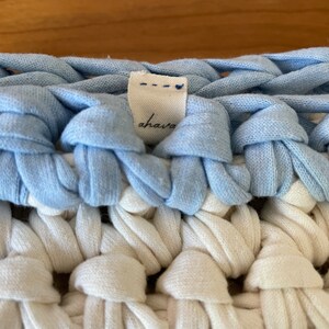 Puede incluir: Primer plano de una manta de crochet azul y blanca con una etiqueta blanca que dice "ahaia".